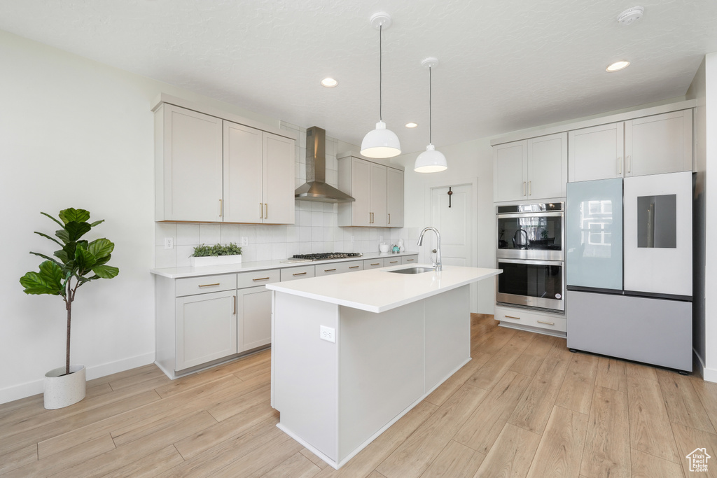 Kitchen with stainless steel appliances, wall chimney exhaust hood, light wood-style flooring, decorative backsplash, and recessed lighting