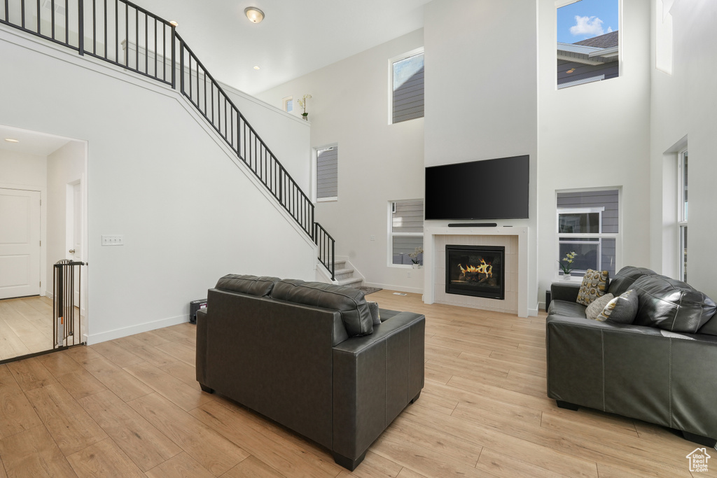Living room featuring a high ceiling, light wood finished floors, plenty of natural light, and a tiled fireplace