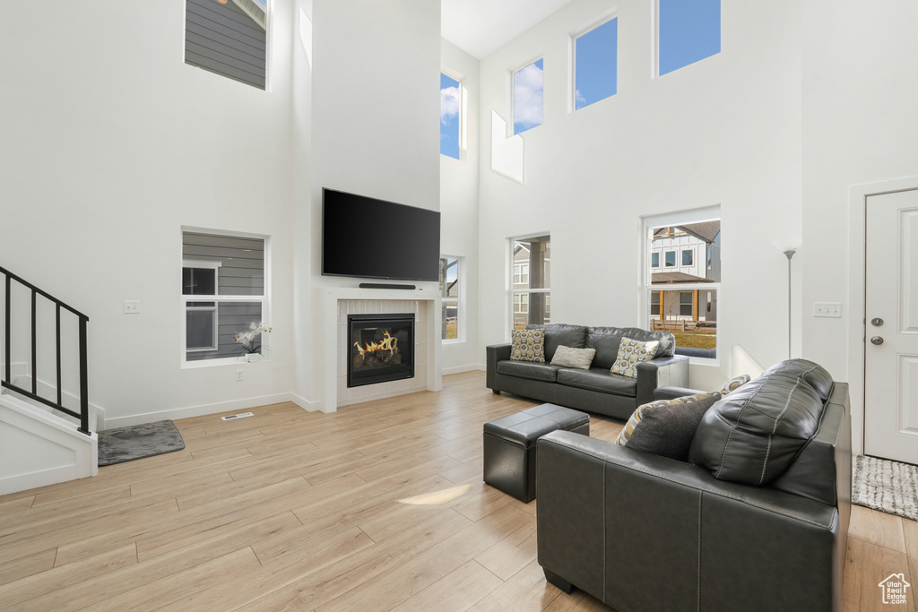 Living room with a towering ceiling, light wood-style flooring, a glass covered fireplace, stairway, and baseboards