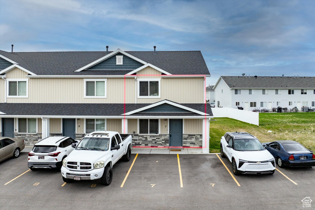 View of front of home with uncovered parking, roof with shingles, stone siding, and a front yard