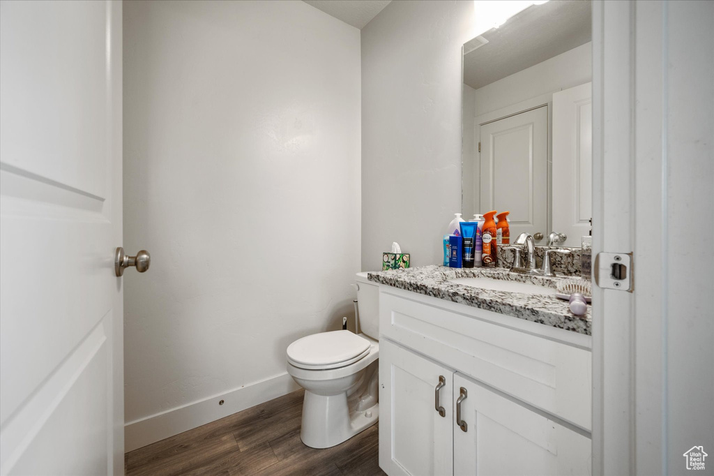 Half bathroom featuring wood finished floors, toilet, vanity, and baseboards