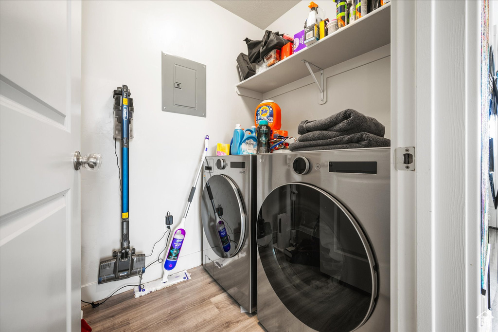 Laundry room with washing machine and dryer, wood finished floors, and electric panel