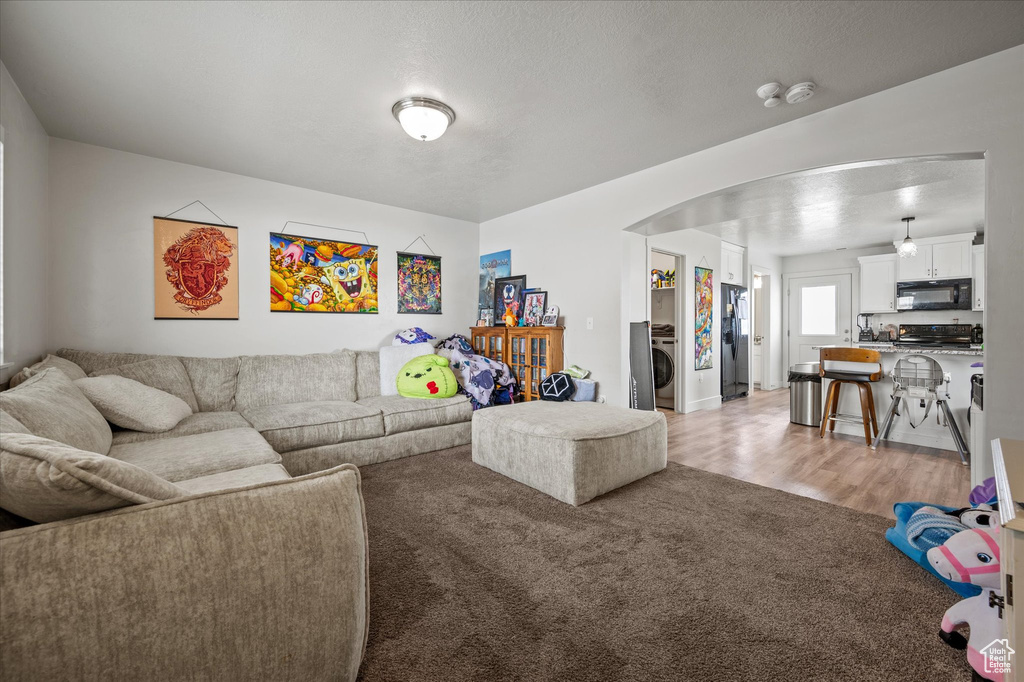 Living room with washer / dryer, arched walkways, light carpet, and light wood-style floors