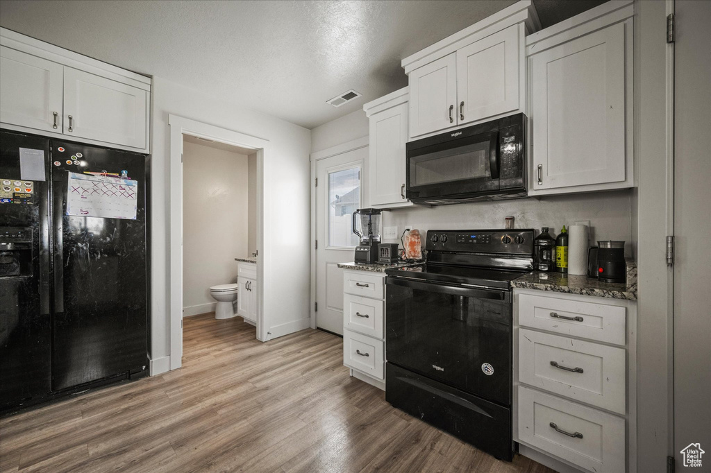 Kitchen featuring black appliances, light wood finished floors, white cabinets, dark stone counters, and baseboards
