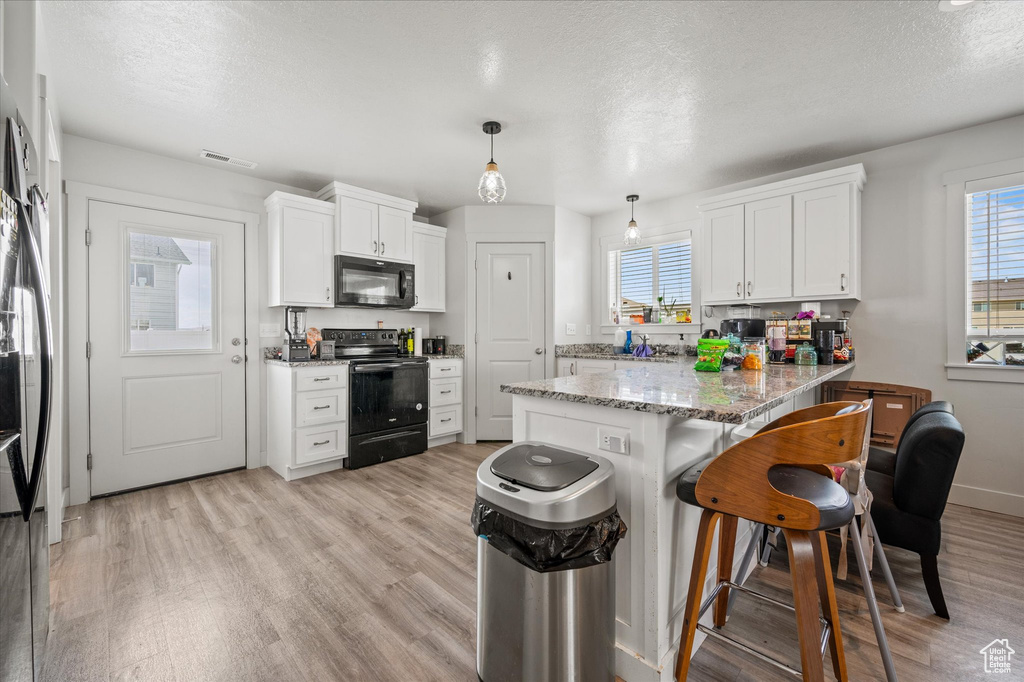 Kitchen with black appliances, a peninsula, a breakfast bar, light wood finished floors, and white cabinets