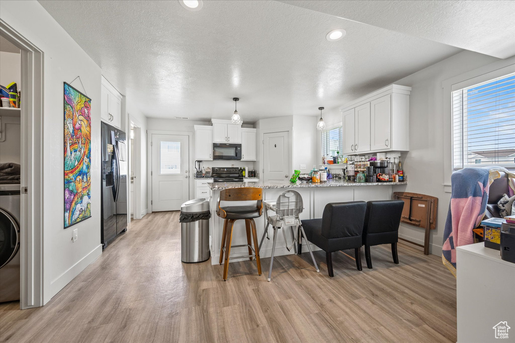 Kitchen featuring black microwave, electric range oven, refrigerator with ice dispenser, a peninsula, and light wood-type flooring