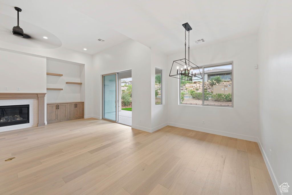 Unfurnished living room featuring a chandelier, light wood-type flooring, a glass covered fireplace, baseboards, and recessed lighting