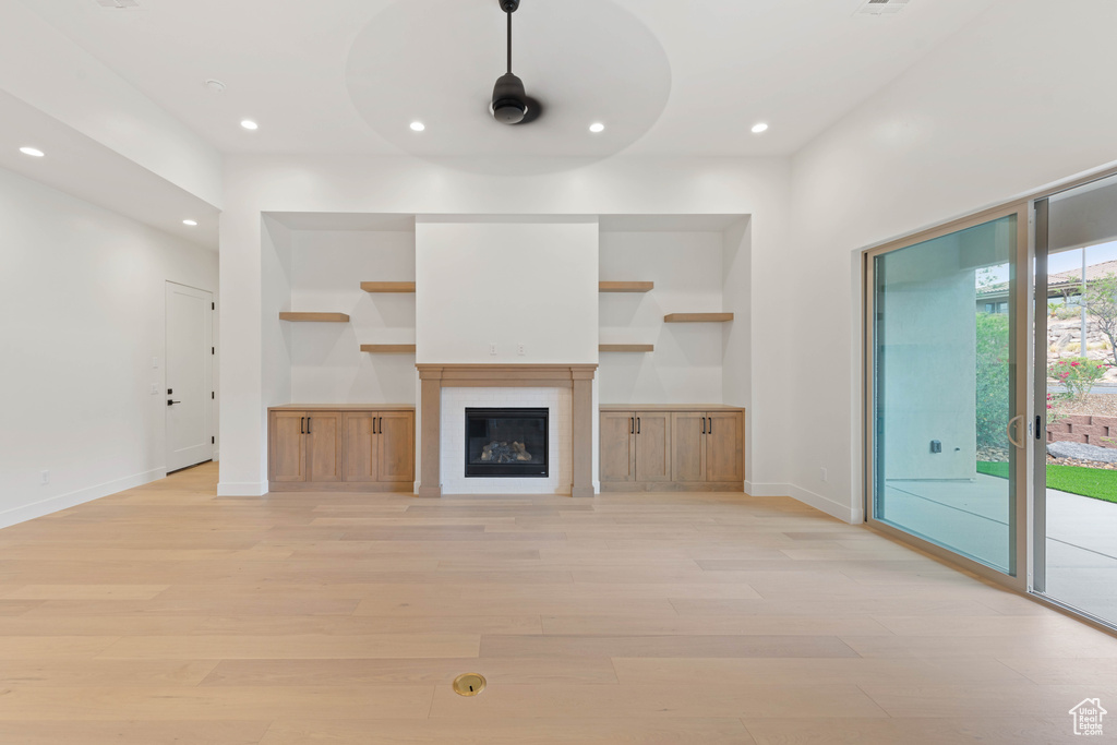 Unfurnished living room with light wood finished floors, recessed lighting, baseboards, built in shelves, and a glass covered fireplace