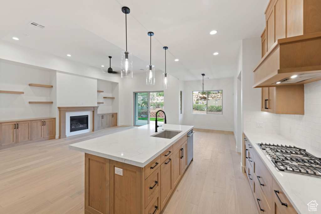 Kitchen with a sink, light wood-style floors, recessed lighting, backsplash, and a kitchen island with sink