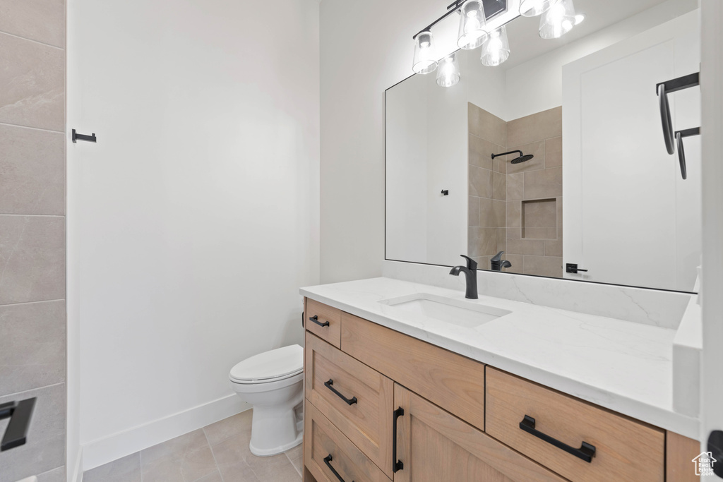 Bathroom with toilet, tiled shower, vanity, baseboards, and tile patterned floors