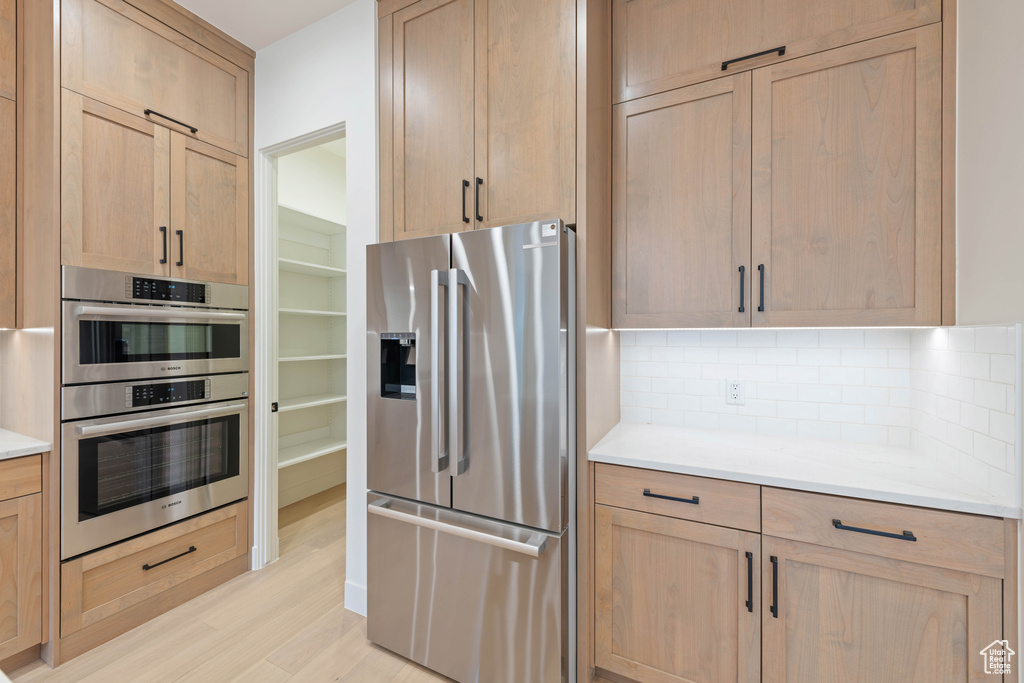 Kitchen with appliances with stainless steel finishes, decorative backsplash, light wood-style flooring, and light brown cabinets