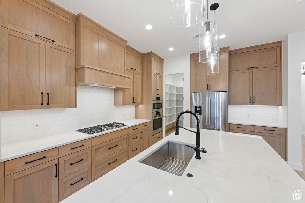 Kitchen with a sink, stainless steel appliances, pendant lighting, decorative backsplash, and light stone countertops