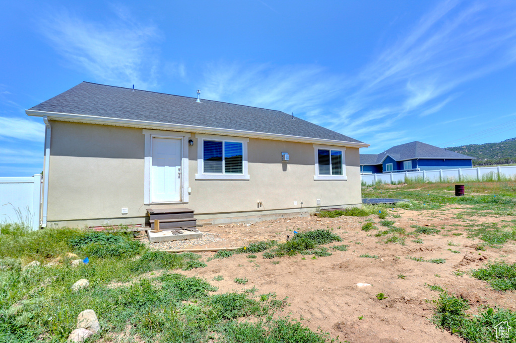 Back of house with entry steps, fence, stucco siding, and roof with shingles