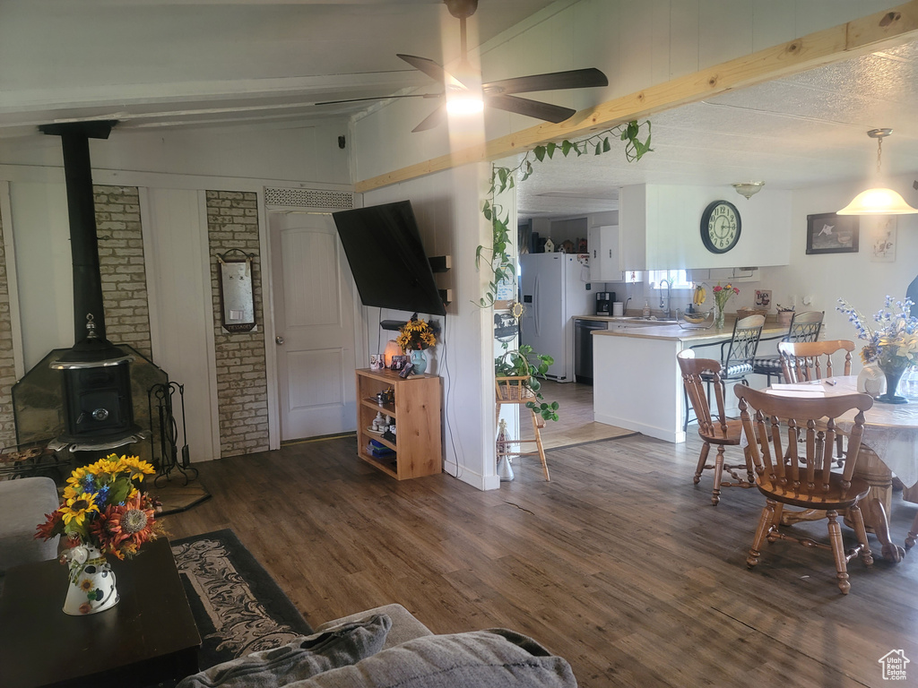 Living room with a wood stove, beamed ceiling, wood finished floors, ceiling fan, and brick wall
