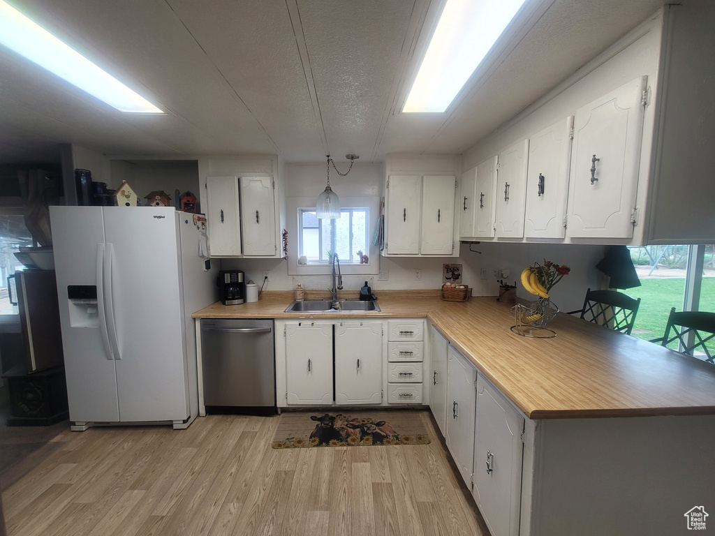 Kitchen featuring white refrigerator with ice dispenser, dishwasher, a sink, light countertops, and light wood-type flooring