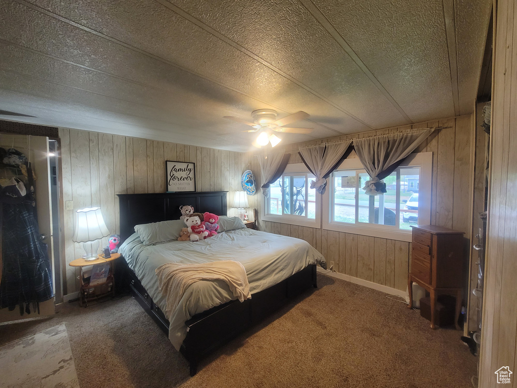 Bedroom with wooden walls, carpet floors, a textured ceiling, baseboards, and a ceiling fan