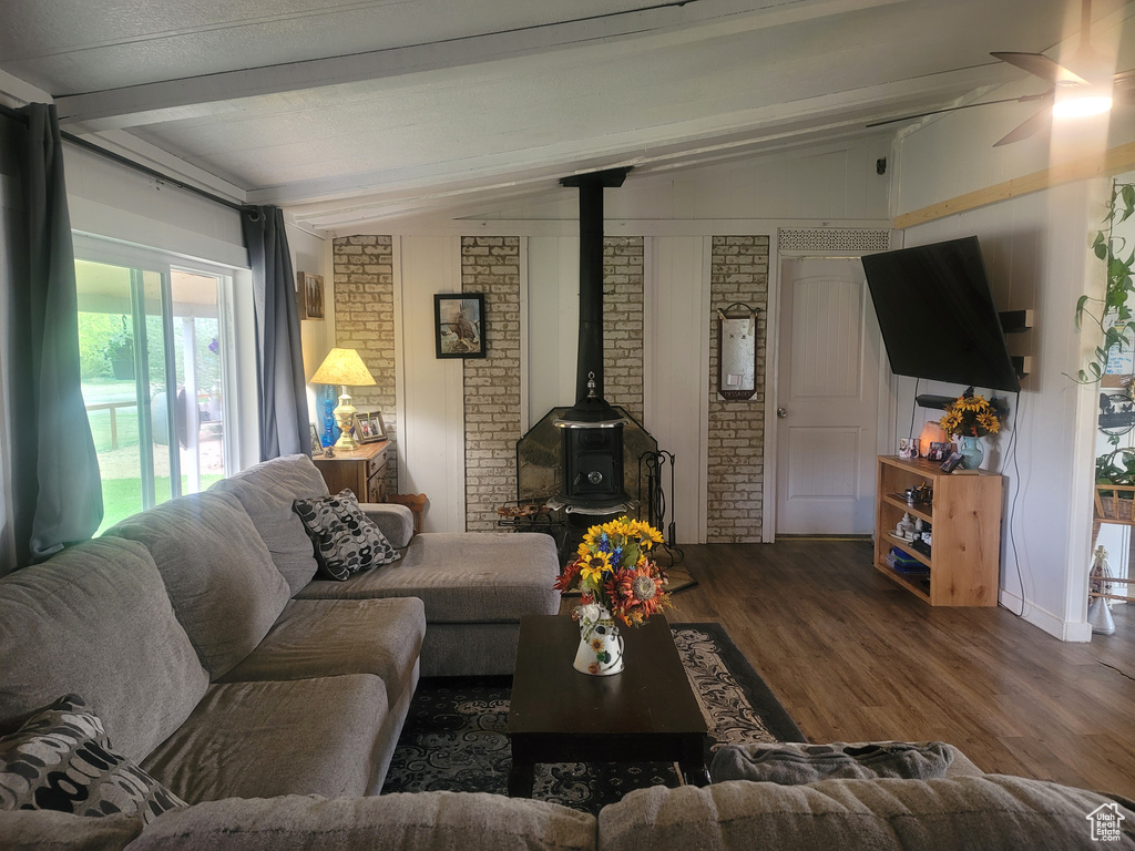 Living area featuring a wood stove, wood finished floors, brick wall, and a ceiling fan