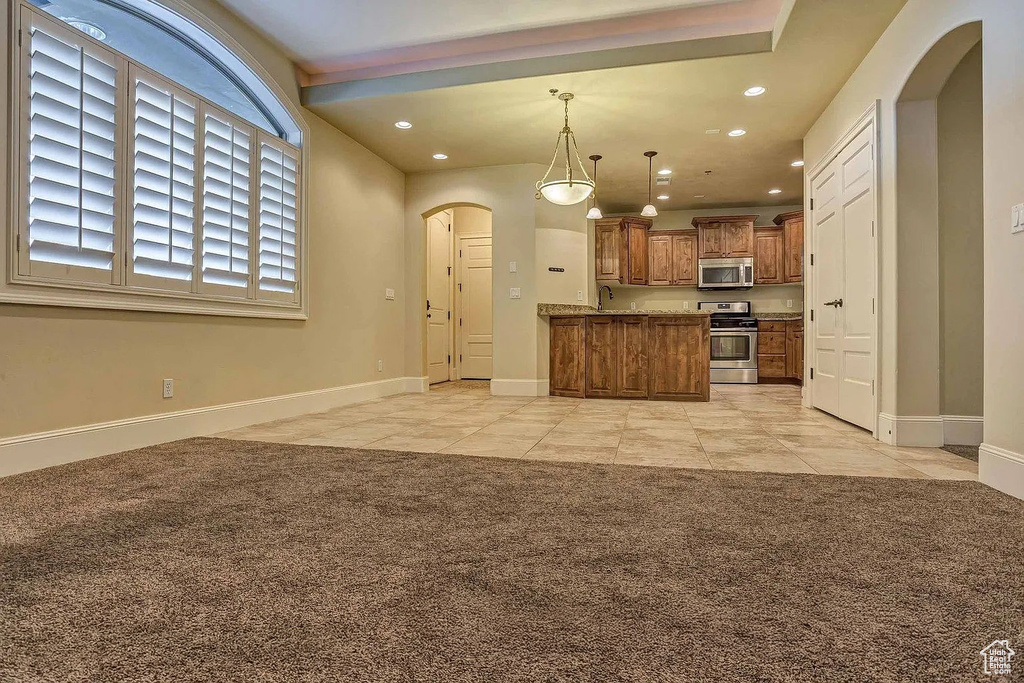 Kitchen featuring stainless steel appliances, arched walkways, brown cabinetry, recessed lighting, and light colored carpet