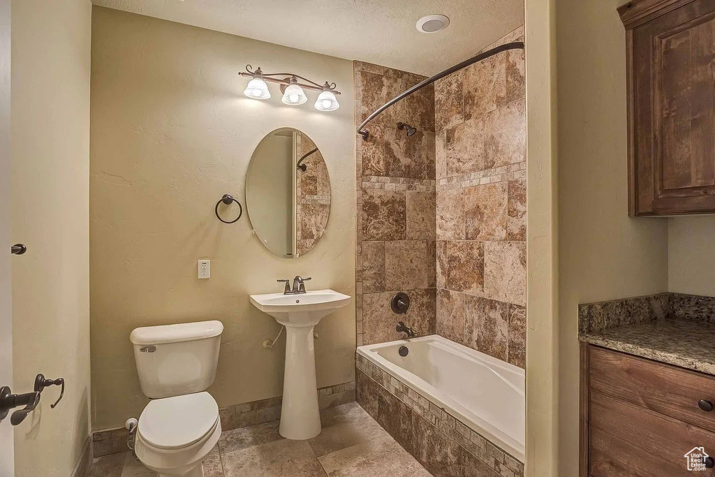 Bathroom with toilet, tiled shower / bath combo, and baseboards