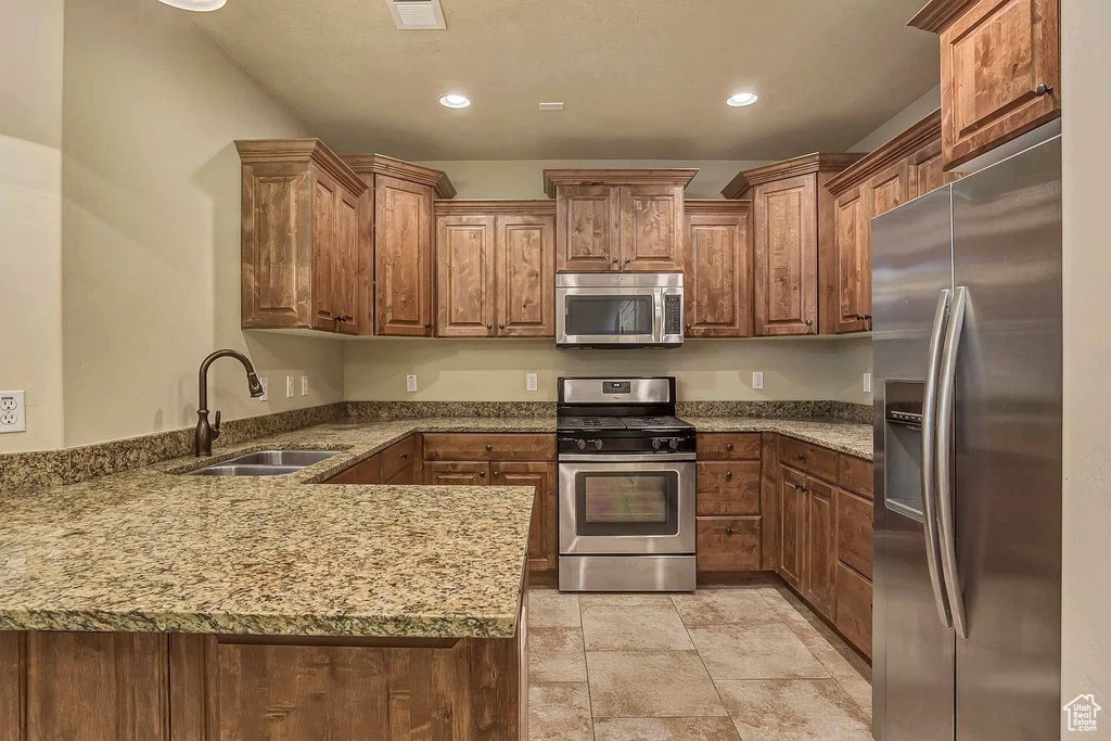 Kitchen featuring stainless steel appliances, a sink, a peninsula, stone countertops, and recessed lighting