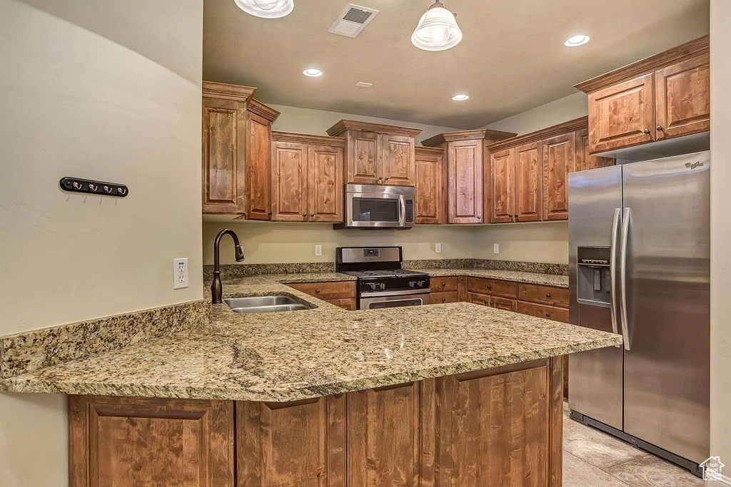 Kitchen with appliances with stainless steel finishes, a sink, a peninsula, light stone counters, and recessed lighting