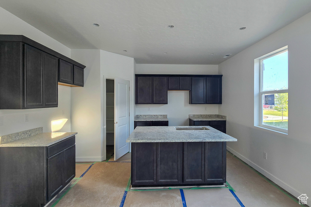 Kitchen featuring baseboards, a kitchen island, light stone counters, and concrete flooring