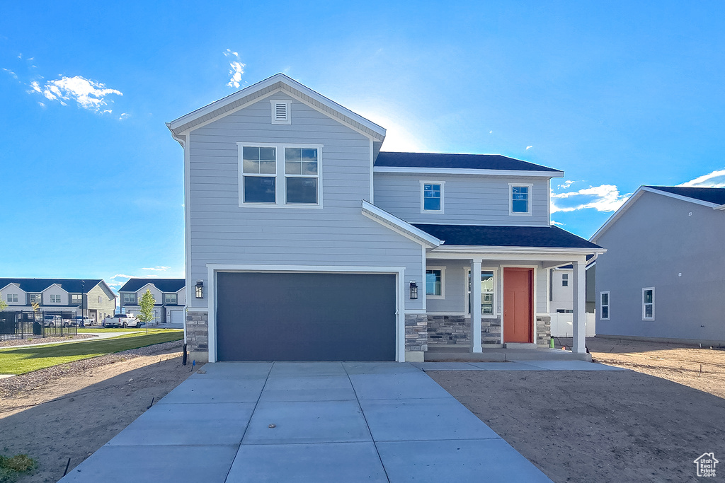 View of front of house with a porch, a garage, driveway, and stone siding