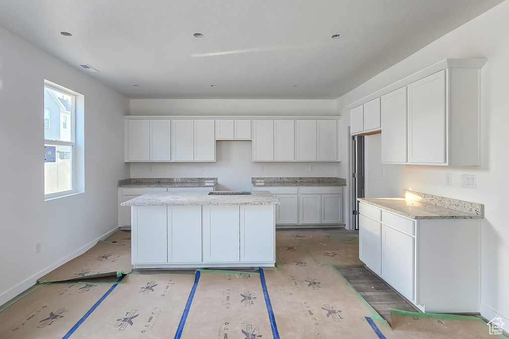 Kitchen featuring a center island, white cabinets, baseboards, stovetop, and light stone counters