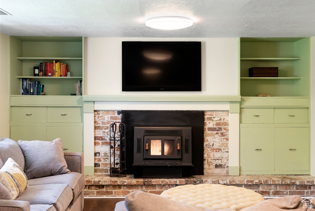 Living area with a textured ceiling, built in features, a brick fireplace, and wood finished floors