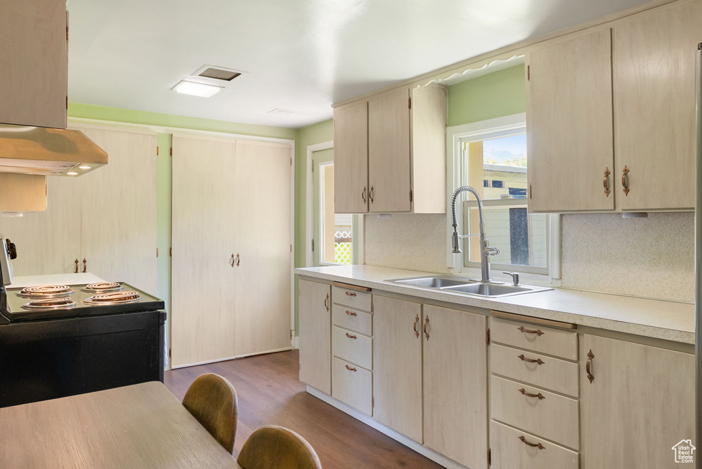 Kitchen with a sink, black range with electric cooktop, light countertops, under cabinet range hood, and light brown cabinetry