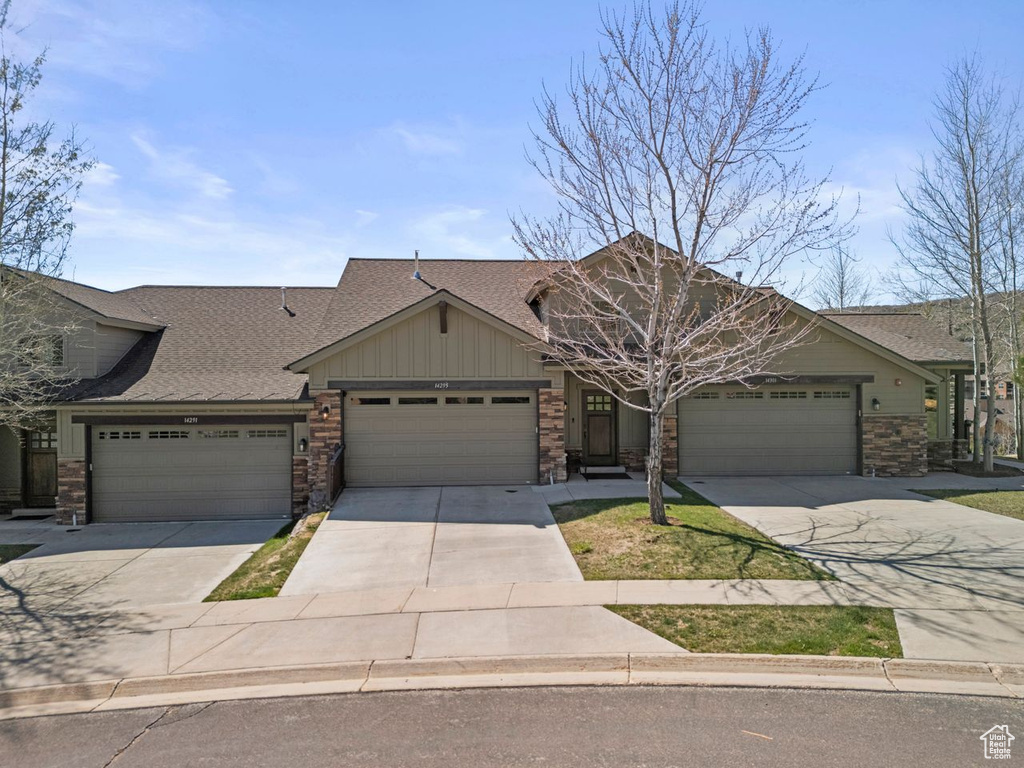 View of front of house featuring an attached garage, stone siding, concrete driveway, board and batten siding, and roof with shingles