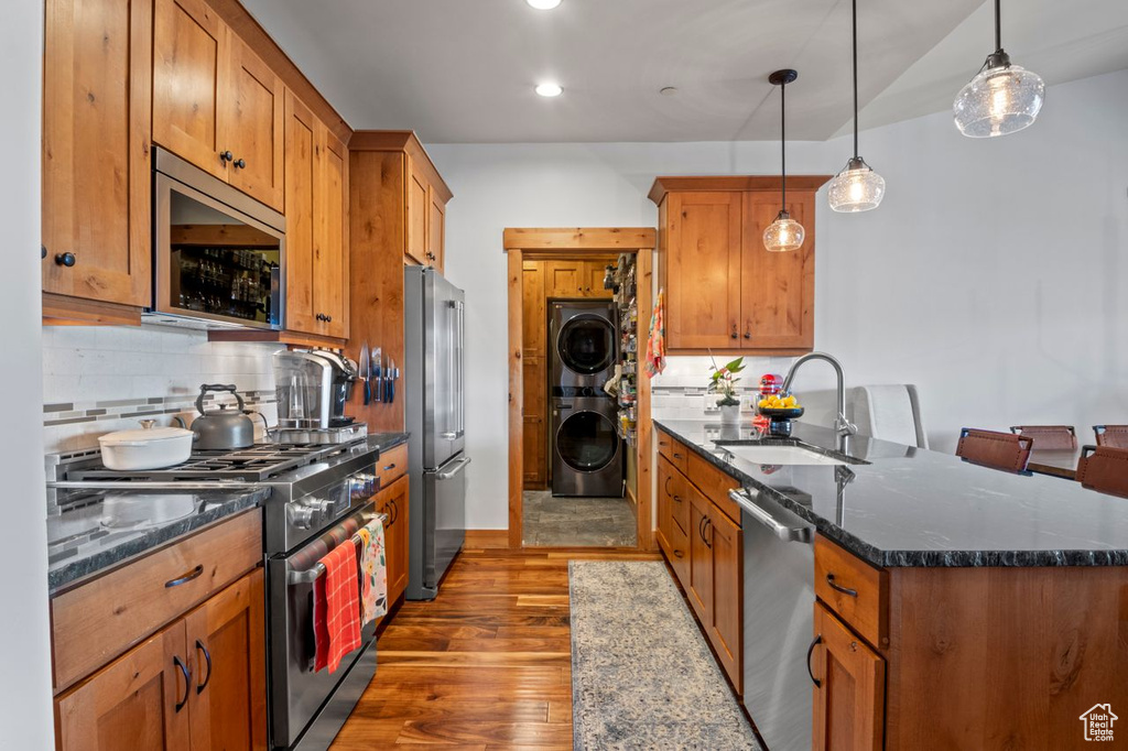 Kitchen featuring a sink, stacked washing maching and dryer, a peninsula, backsplash, and stainless steel appliances
