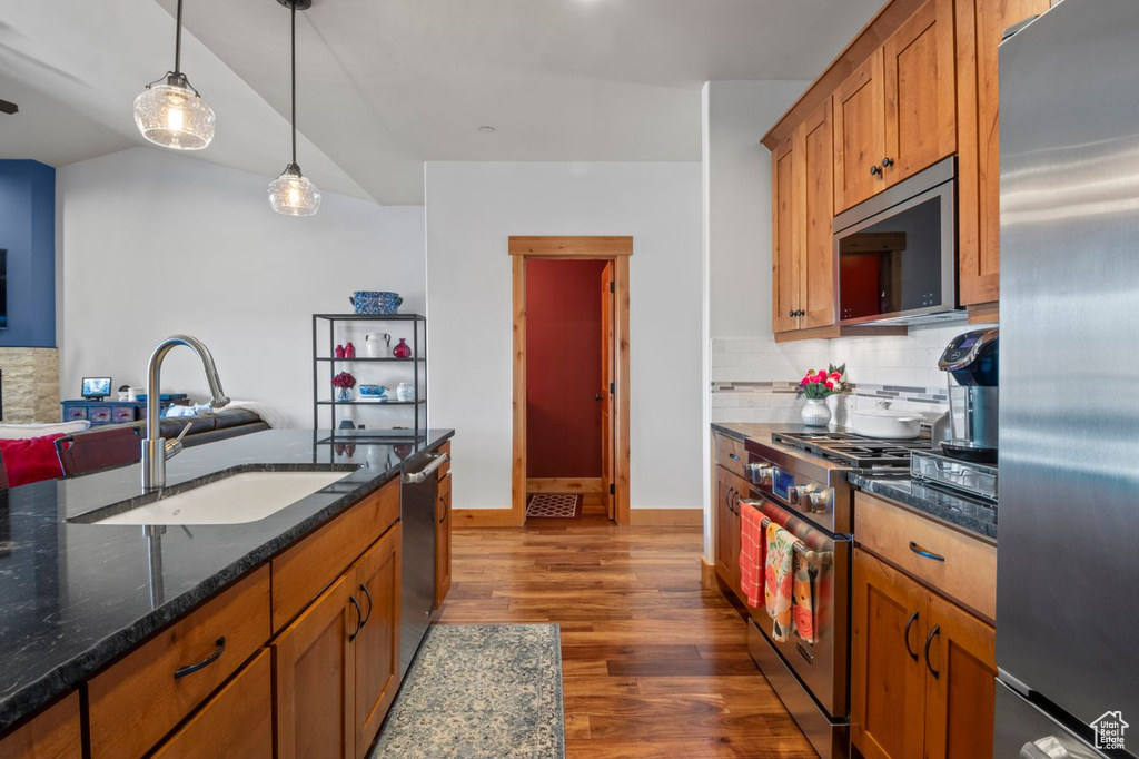 Kitchen with brown cabinetry, a sink, decorative backsplash, dark wood-type flooring, and appliances with stainless steel finishes