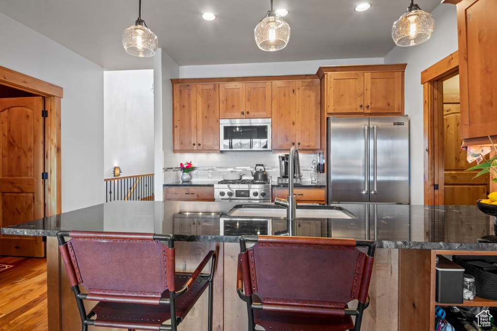 Kitchen with wood finished floors, a sink, decorative light fixtures, appliances with stainless steel finishes, and decorative backsplash
