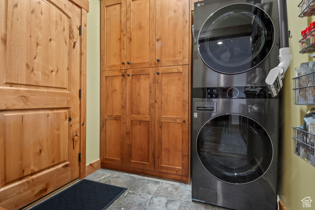 Clothes washing area with baseboards, stacked washer and dryer, stone finish flooring, and cabinet space