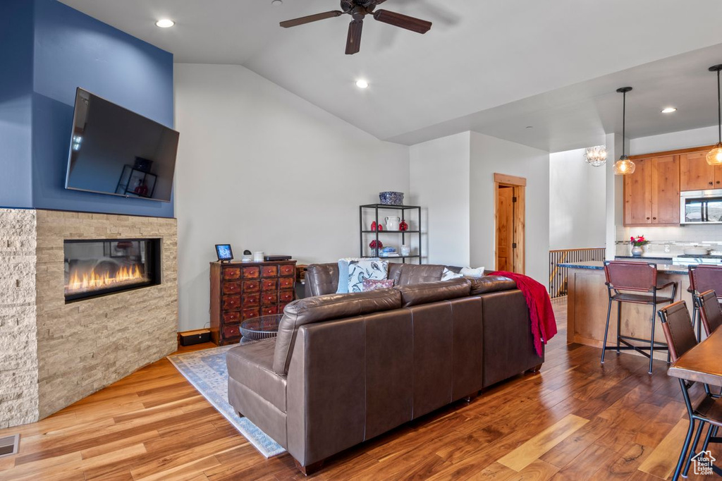 Living area with a ceiling fan, lofted ceiling, a stone fireplace, visible vents, and wood finished floors