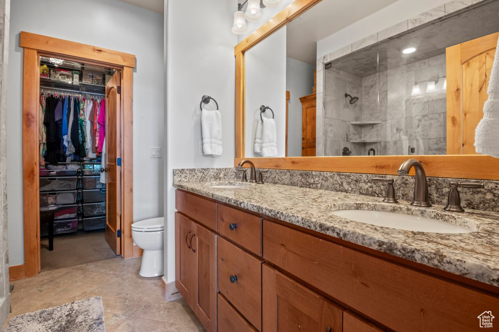 Bathroom with double vanity, toilet, a tile shower, a sink, and a walk in closet