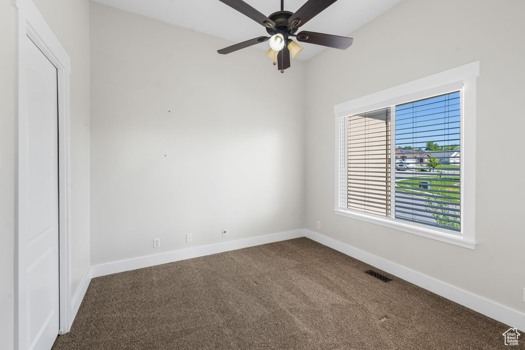 Spare room with dark colored carpet, baseboards, and a ceiling fan