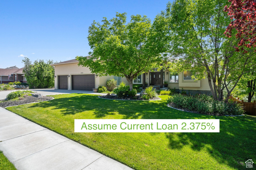 View of property hidden behind natural elements featuring stucco siding, a front yard, an attached garage, and driveway