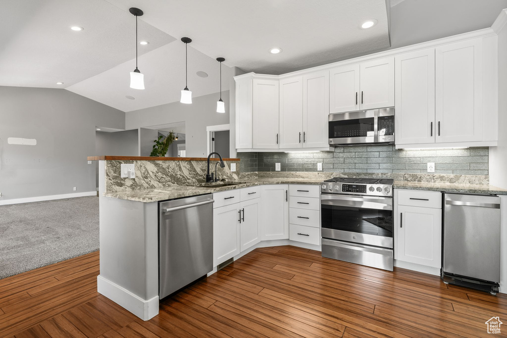 Kitchen featuring appliances with stainless steel finishes, a sink, lofted ceiling, a peninsula, and white cabinetry
