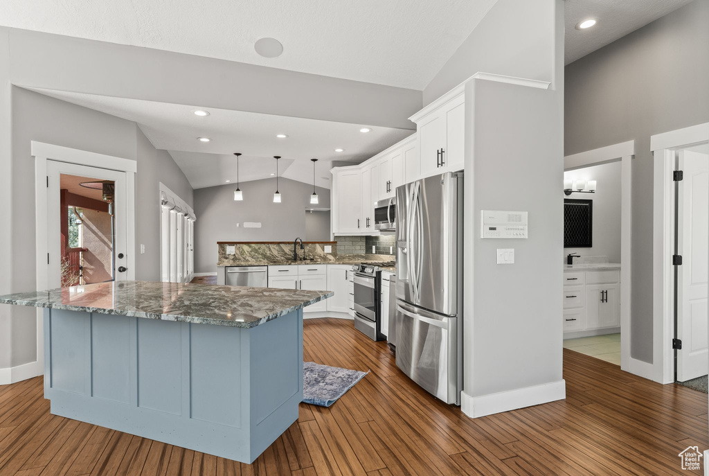 Kitchen with appliances with stainless steel finishes, vaulted ceiling, dark stone counters, dark wood-style floors, and white cabinetry
