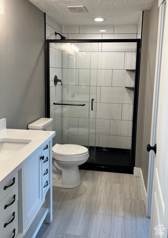 Bathroom with a textured ceiling, vanity, toilet, and a shower stall