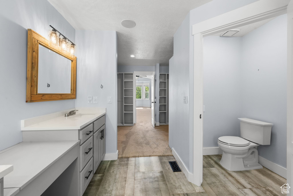 Full bathroom featuring wood finished floors, toilet, vanity, baseboards, and a textured ceiling
