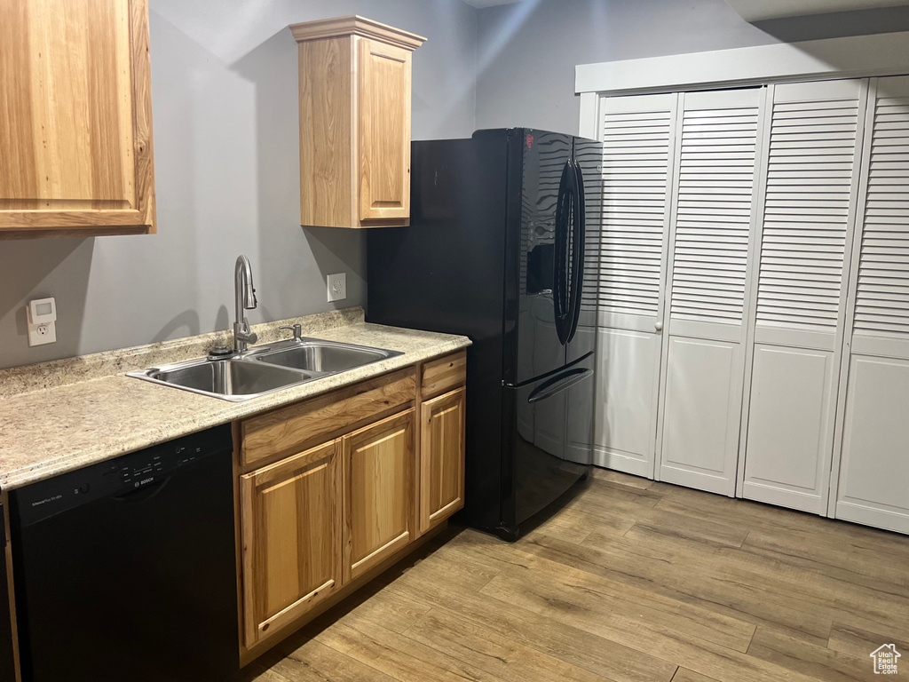 Kitchen featuring black appliances, a sink, light wood-style flooring, and light countertops