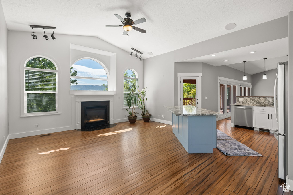 Unfurnished living room with ceiling fan, vaulted ceiling, a fireplace with flush hearth, dark wood finished floors, and baseboards