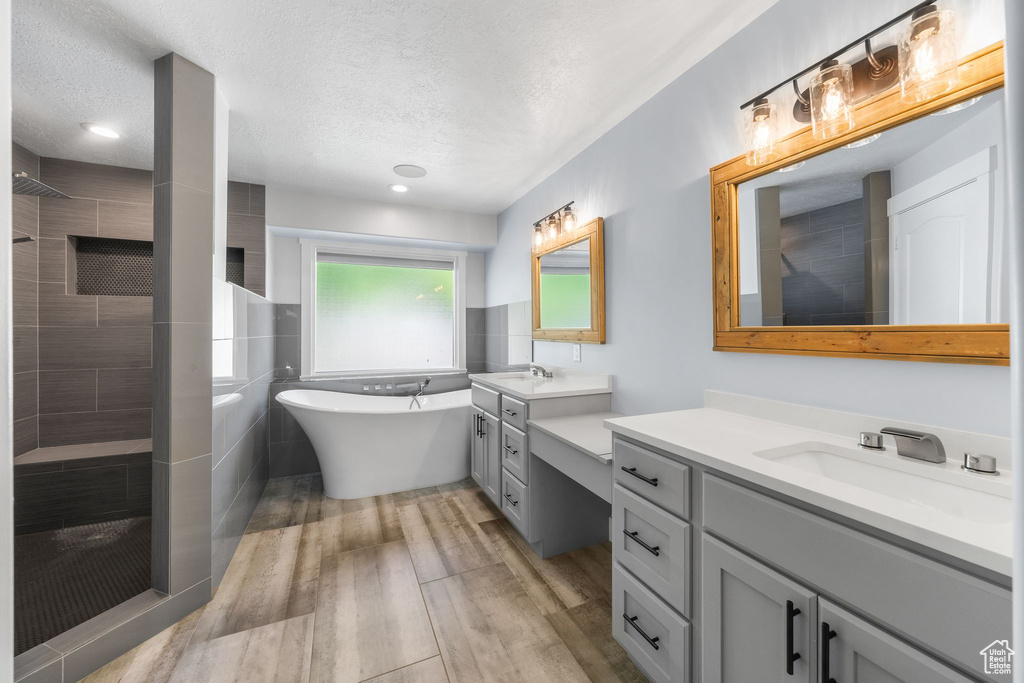 Bathroom featuring a walk in shower, wood finished floors, a freestanding bath, two vanities, and a textured ceiling