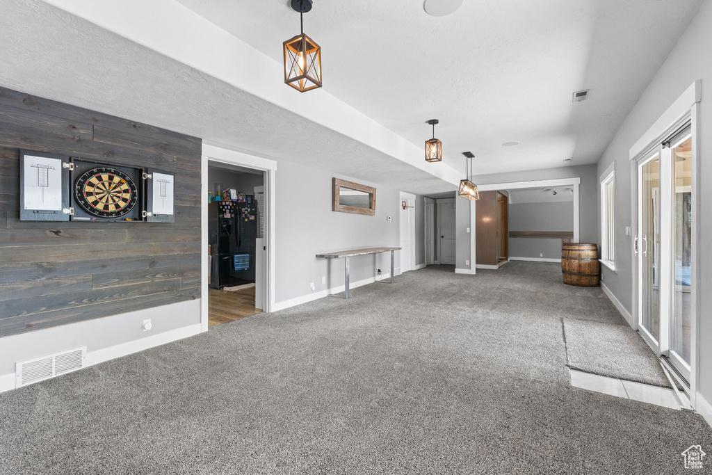 Unfurnished living room featuring carpet flooring, an accent wall, baseboards, and wooden walls