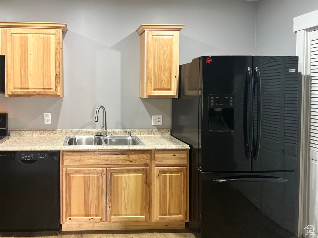 Kitchen featuring black appliances, a sink, light countertops, and light brown cabinets