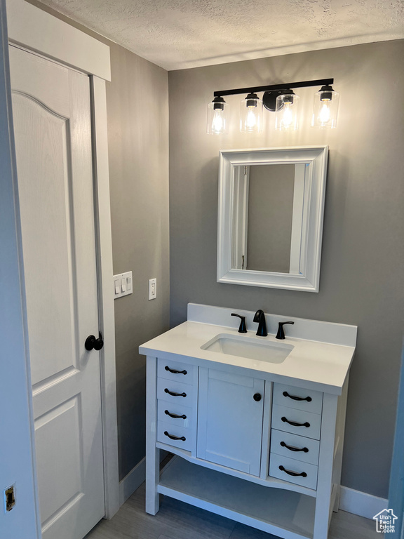 Bathroom with baseboards, a textured ceiling, vanity, and wood finished floors