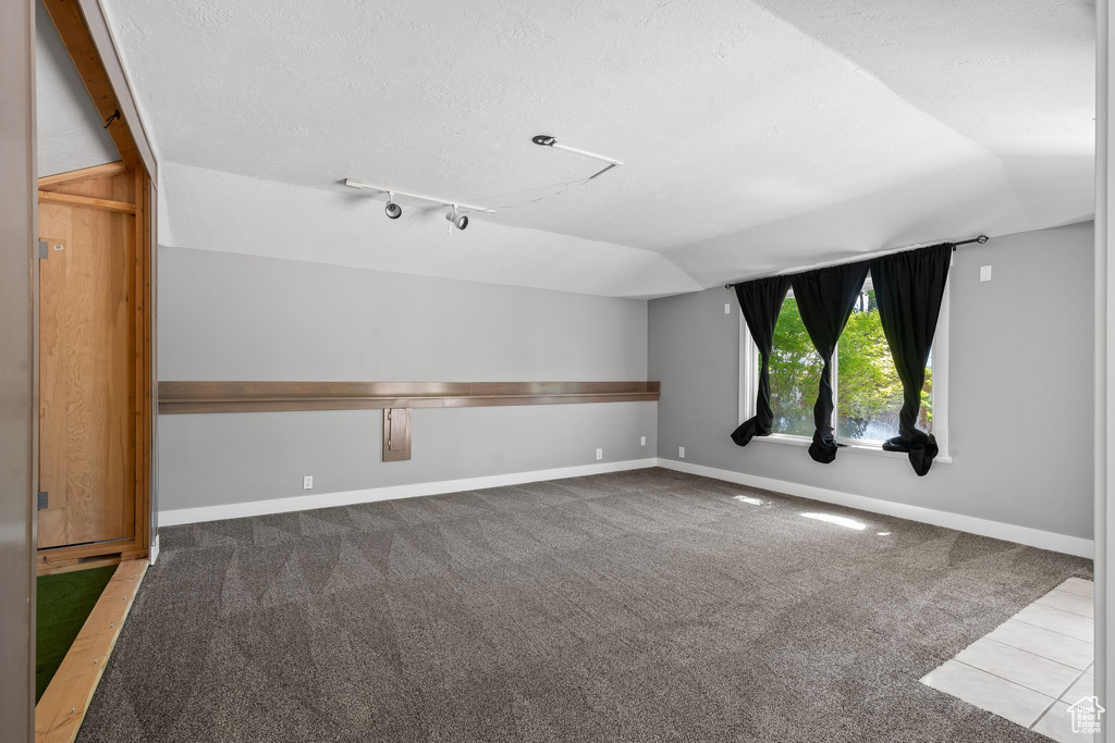 Carpeted empty room with lofted ceiling, track lighting, a textured ceiling, and baseboards